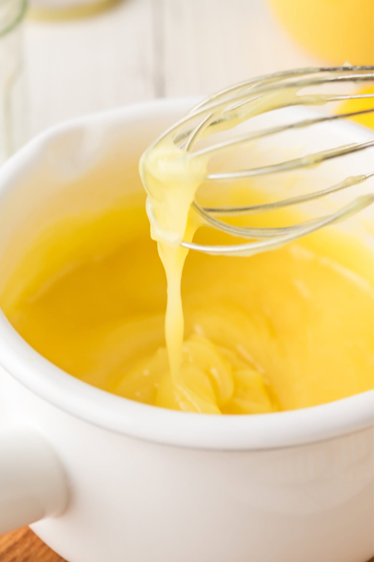 cooked bright yellow lemon curd in a pan with a metal whisk taking some out.