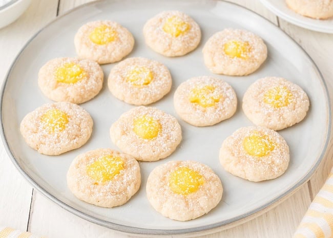 Lemon Thumbprint Cookies sprinkled with powdered sugar on round large plate.