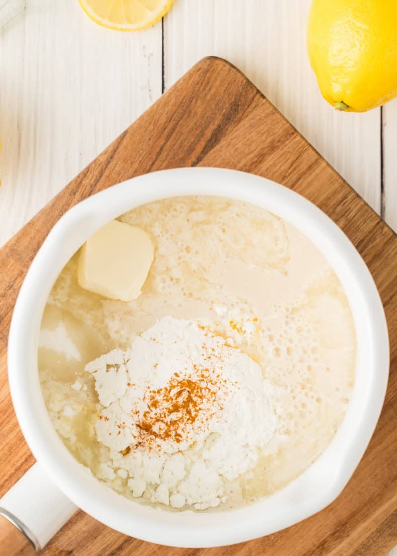 ingredients in a round white cooking pan on a table beside some fresh whole lemons.