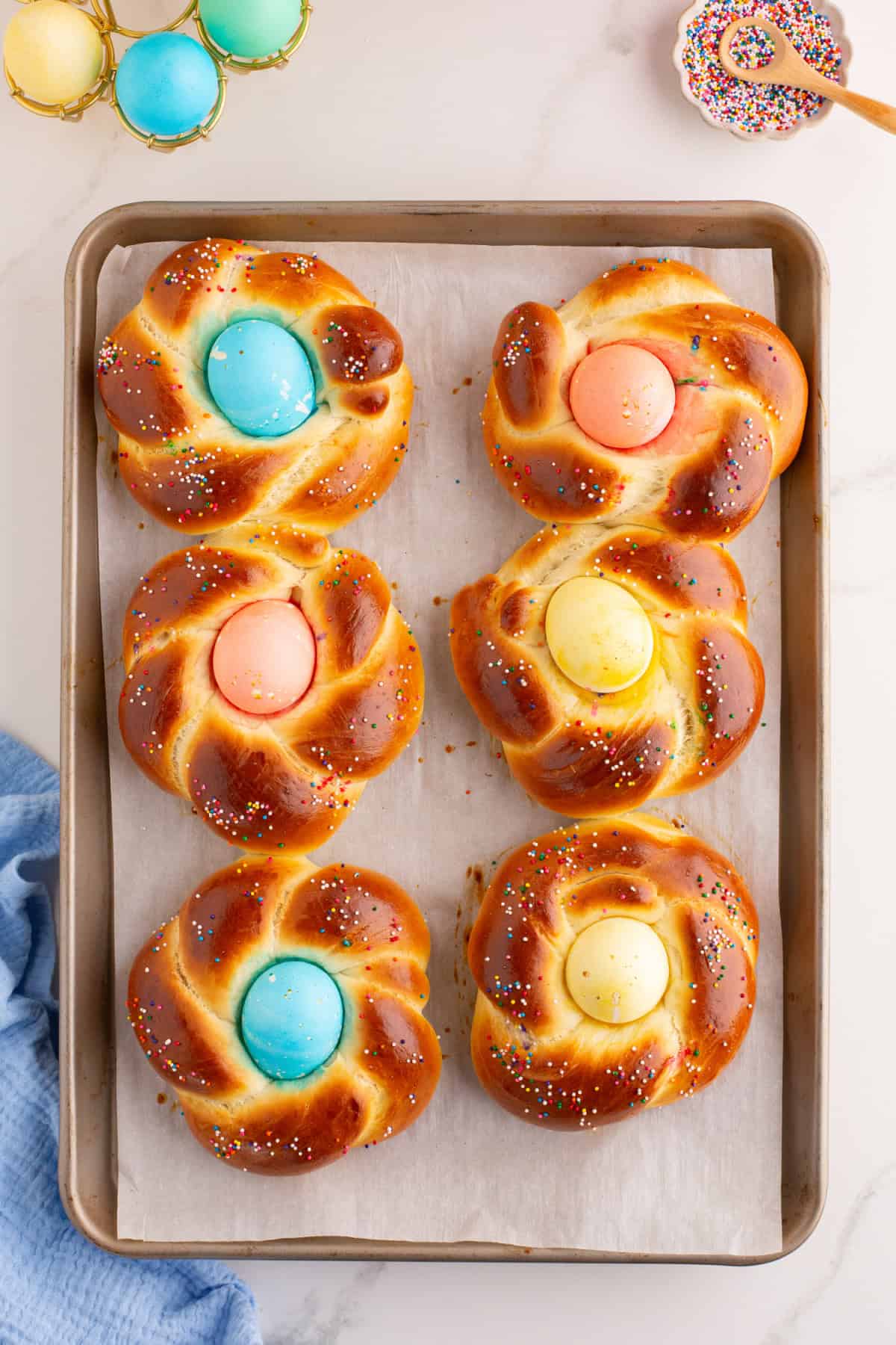 baked easter bread with colored sprinkles and a dyed egg in the middle.