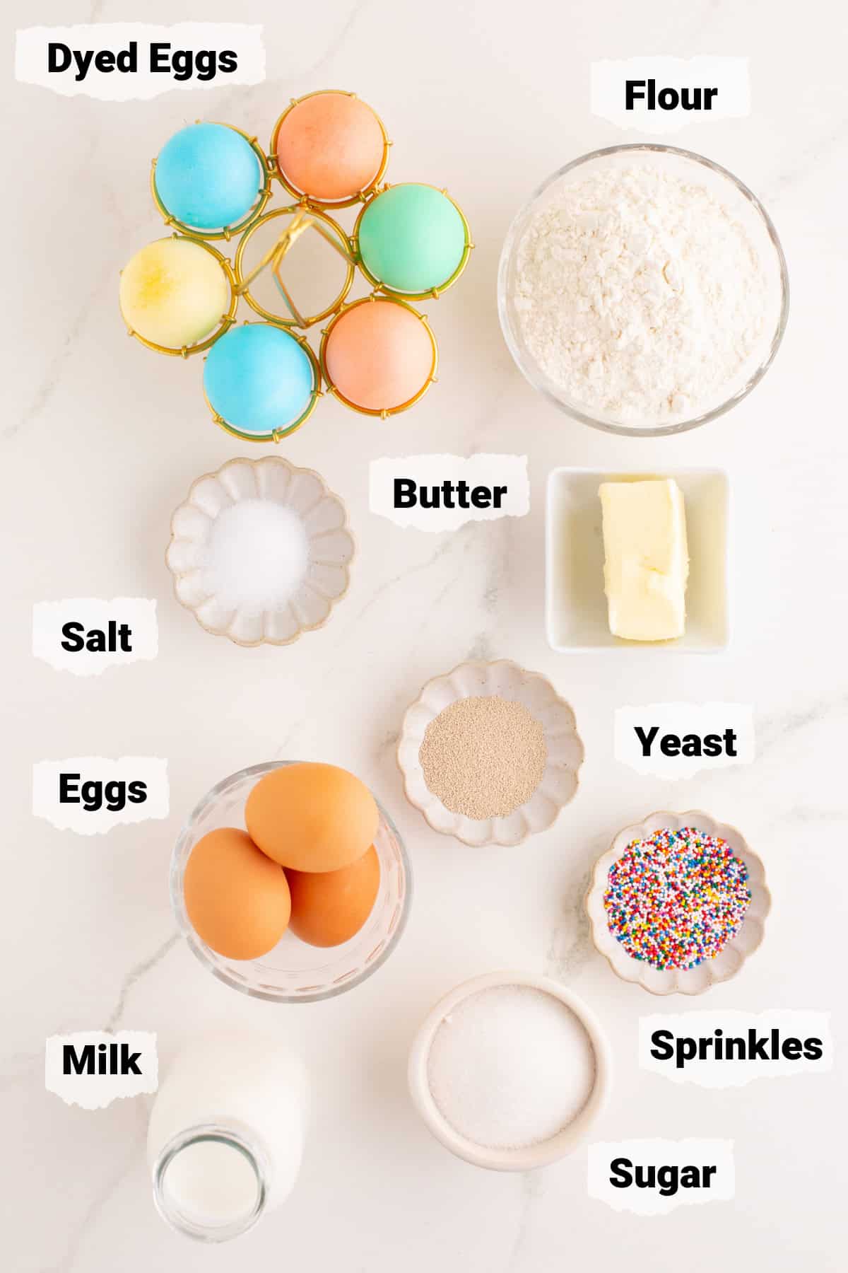 ingredients to make easter bread including flour, year, butter, eggs, milk, and dyed eggs.