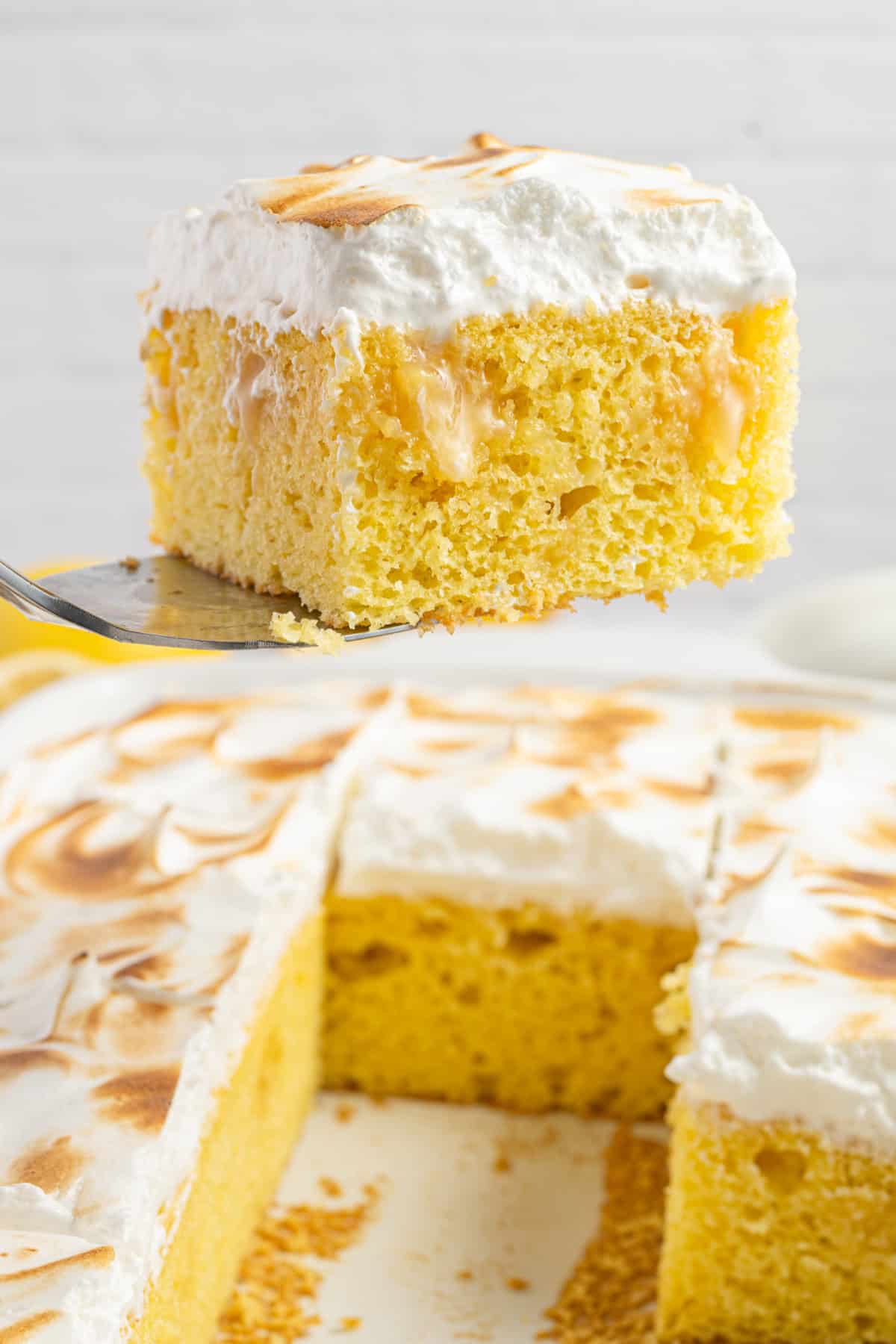 a slice of lemon cake being lifted from a cake using a spatula.