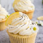 Lemon poppyseed cupcakes with a white buttercream icing on top, sprinkled with poppy seeds and a fresh lemon wedge on top.