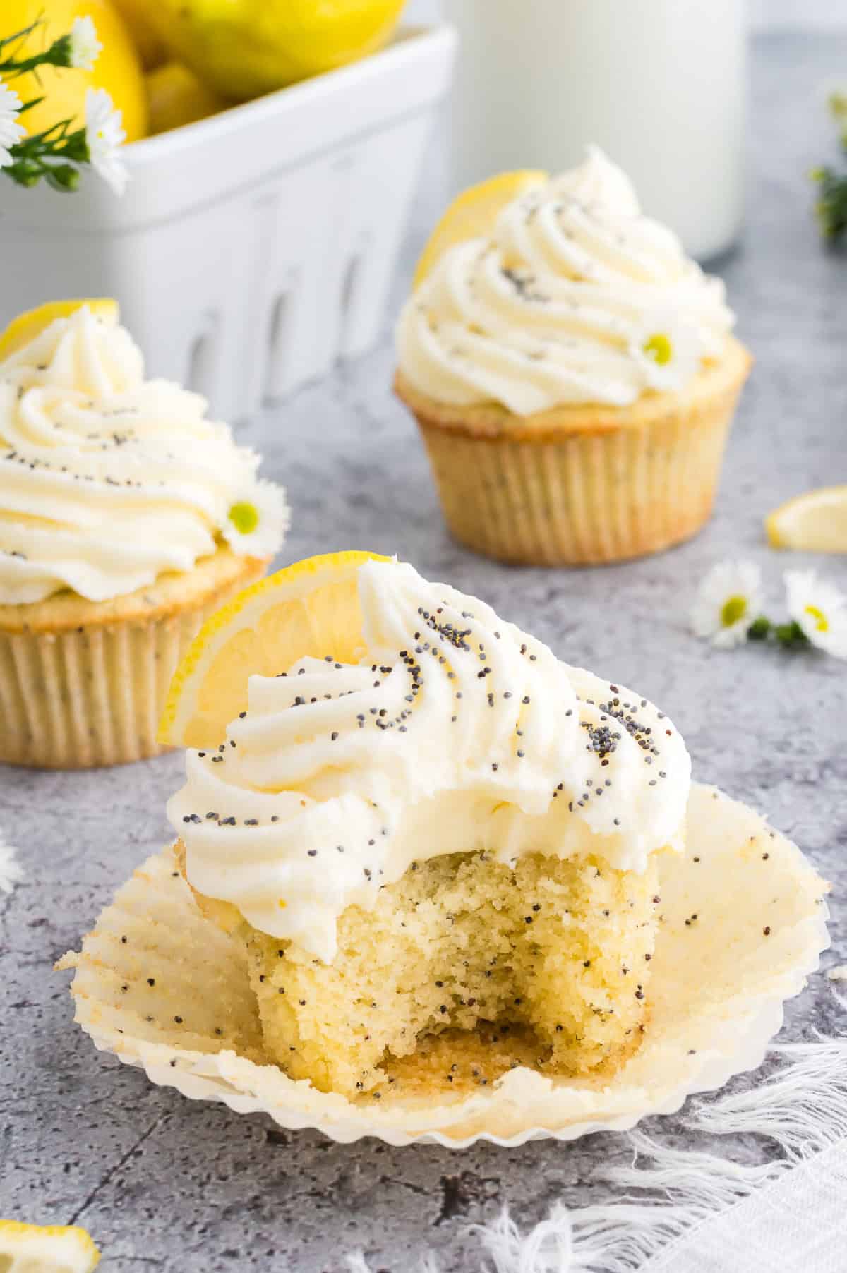 Lemon poppyseed cupcakes with a white buttercream icing on top, sprinkled with poppy seeds and a fresh lemon wedge on top.