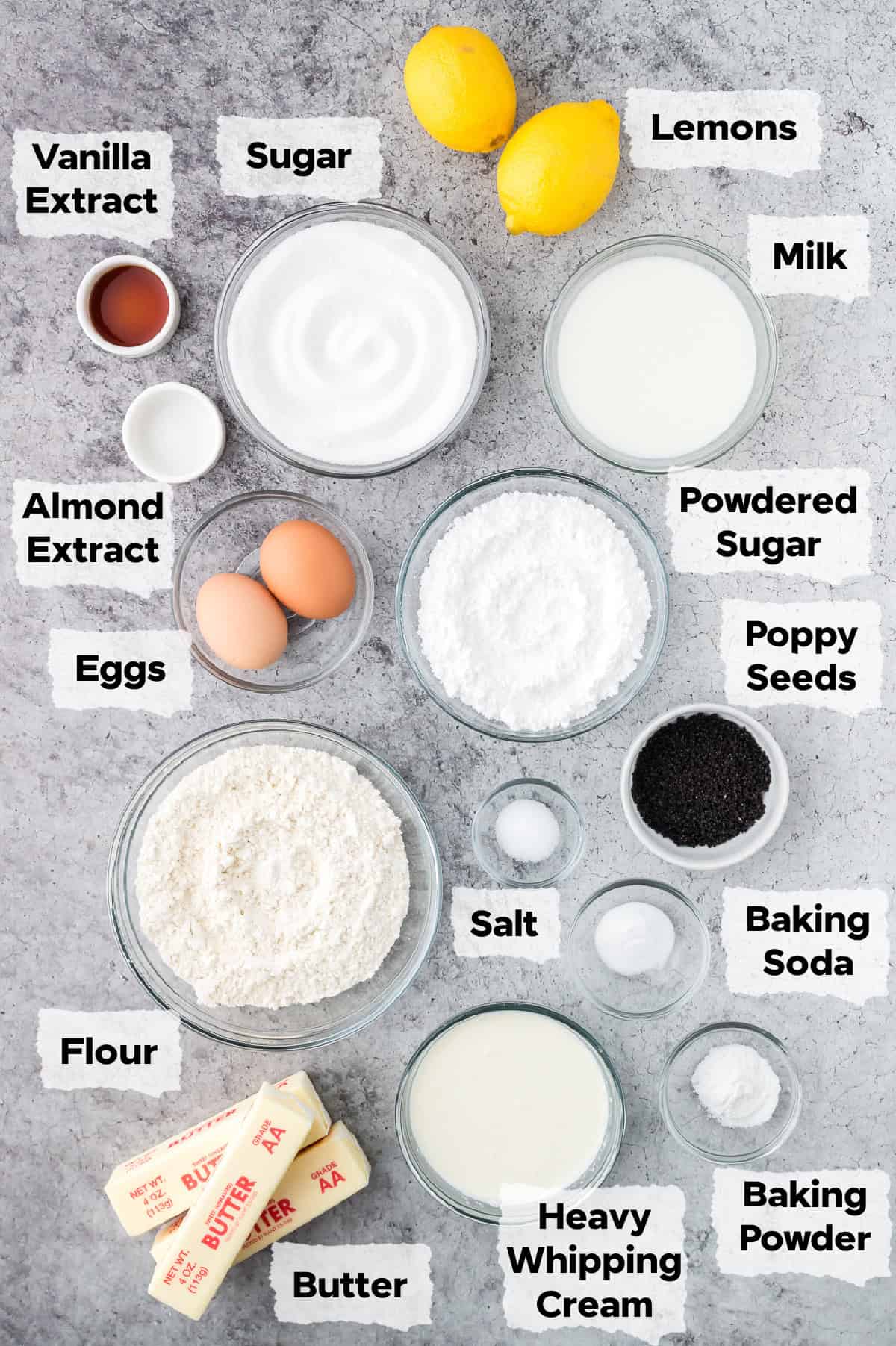 ingredients on a table to make lemon poppy seed cupcakes such as flour, lemons, sugar, poppy seed, eggs, salt and butter.