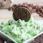 green dessert dip with chocolate dips in a bowl with a whole oreo cookie placed on top.