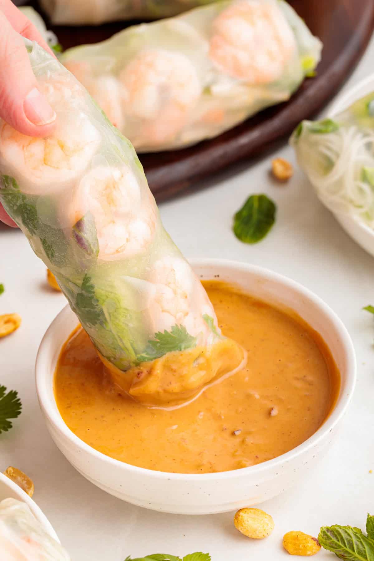 Vietnamese Shrimp Salad Roll being dipped into a small bowl of peanut dipping sauce.