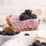 a slice of blackberry cream pie with fresh blackberries on top being taken out of a whole pie.