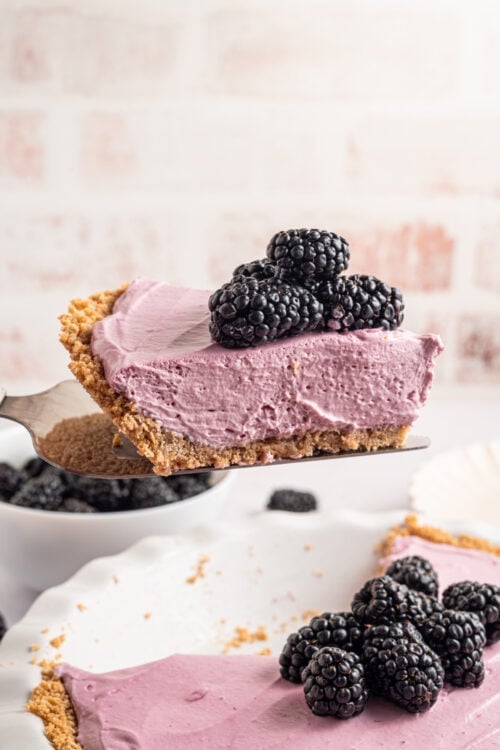a slice of blackberry cream pie with fresh blackberries on top being taken out of a whole pie.