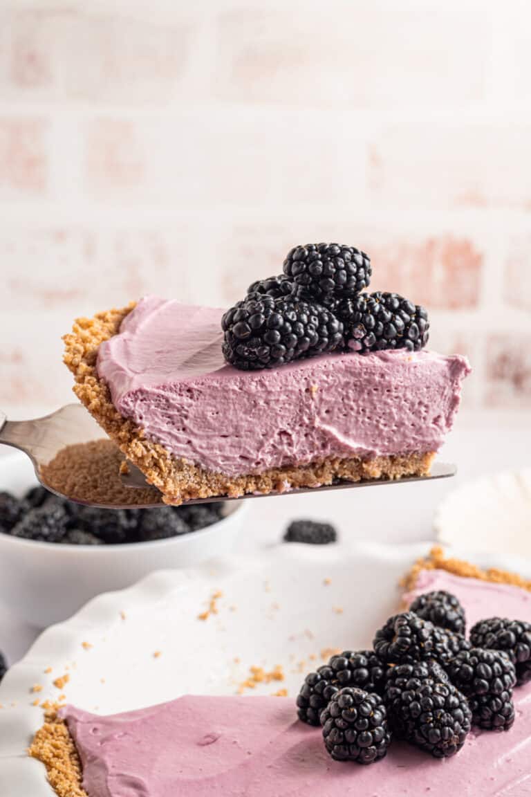 a slice of blackberry cream pie with fresh blackberries on top being taken out of a whole pie.