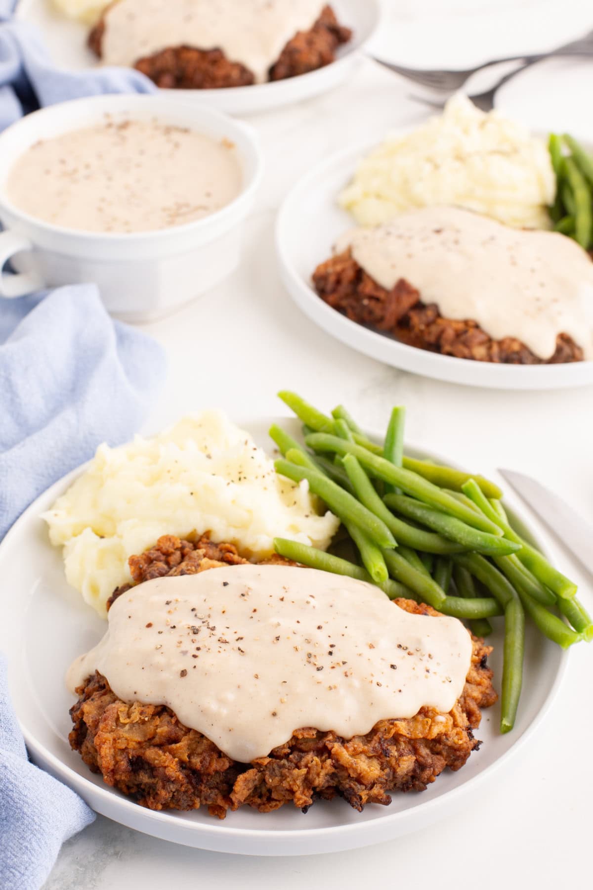 plates of chicken fried steak with gravy on top of it, with mashed potatoes and green beans.