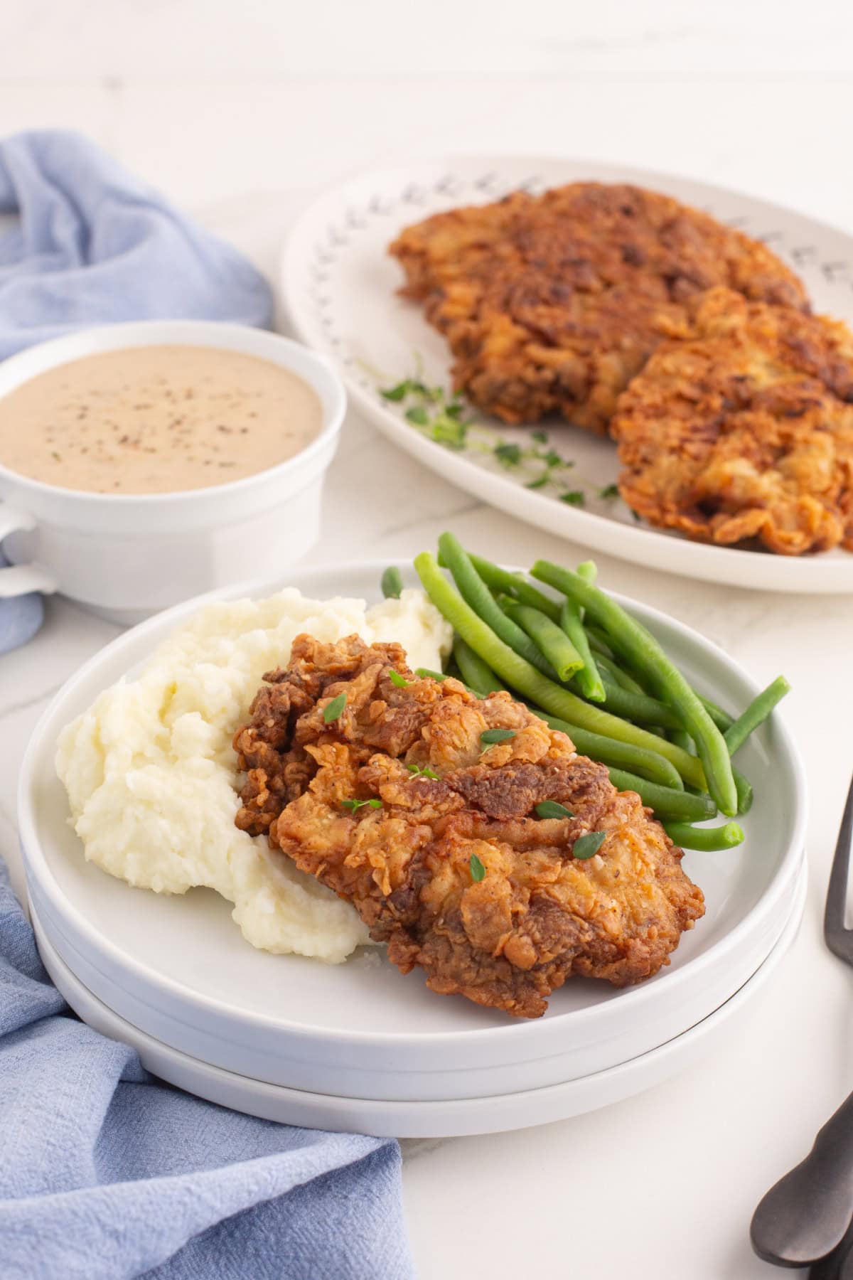 chicken fried steak with a bowl of gravy on the side, on a plate with mashed potatoes and green beans.