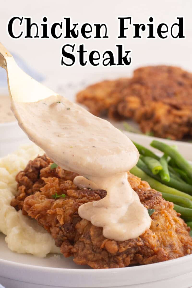 white gravy being pored onto chicken fried steak on a plate with mashed potatoes and green beans.