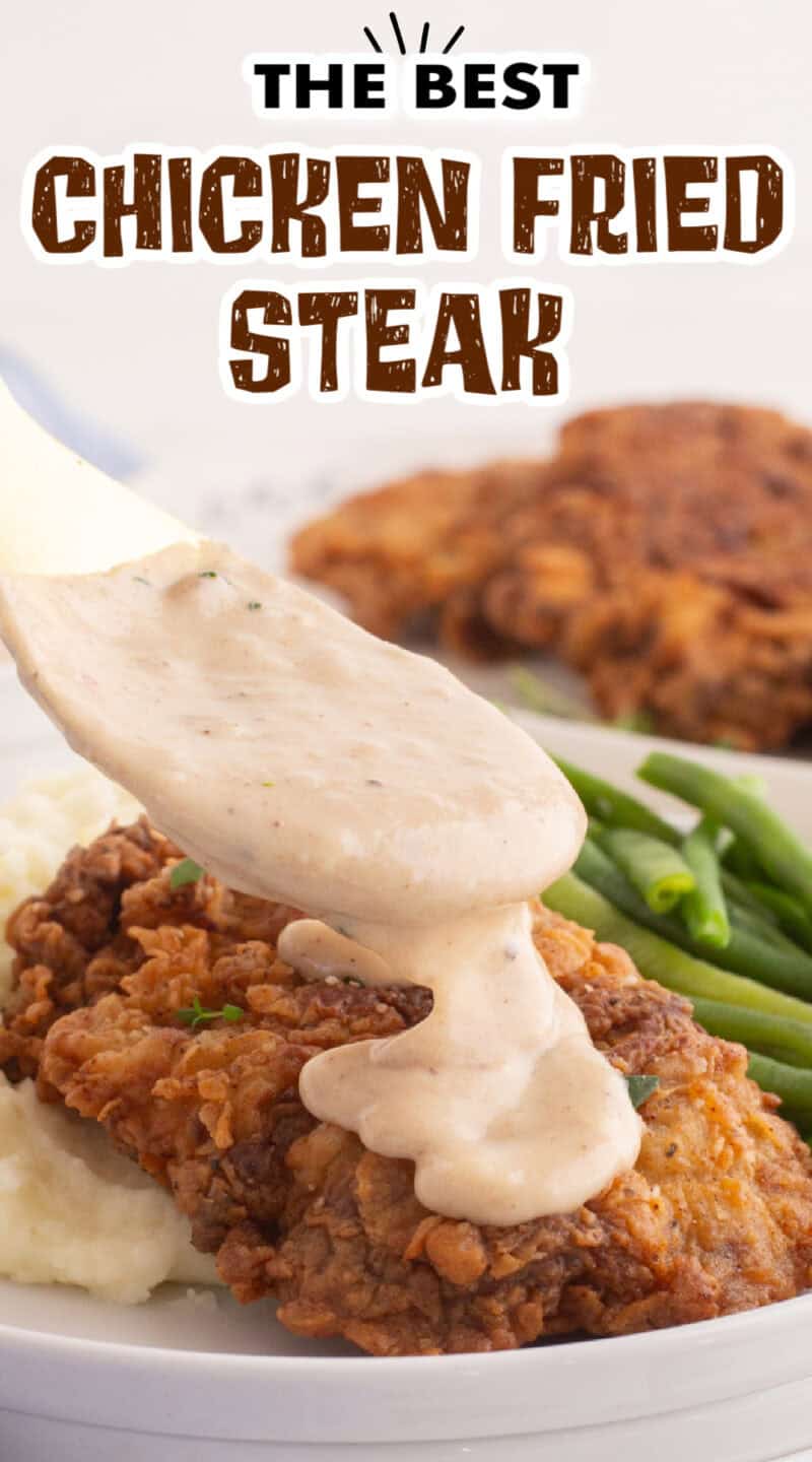 white gravy being pored onto chicken fried steak on a plate with mashed potatoes and green beans.