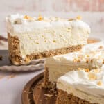A slice of coconut cheesecake being taken out of a whole cheesecake sitting on a wooden plate.