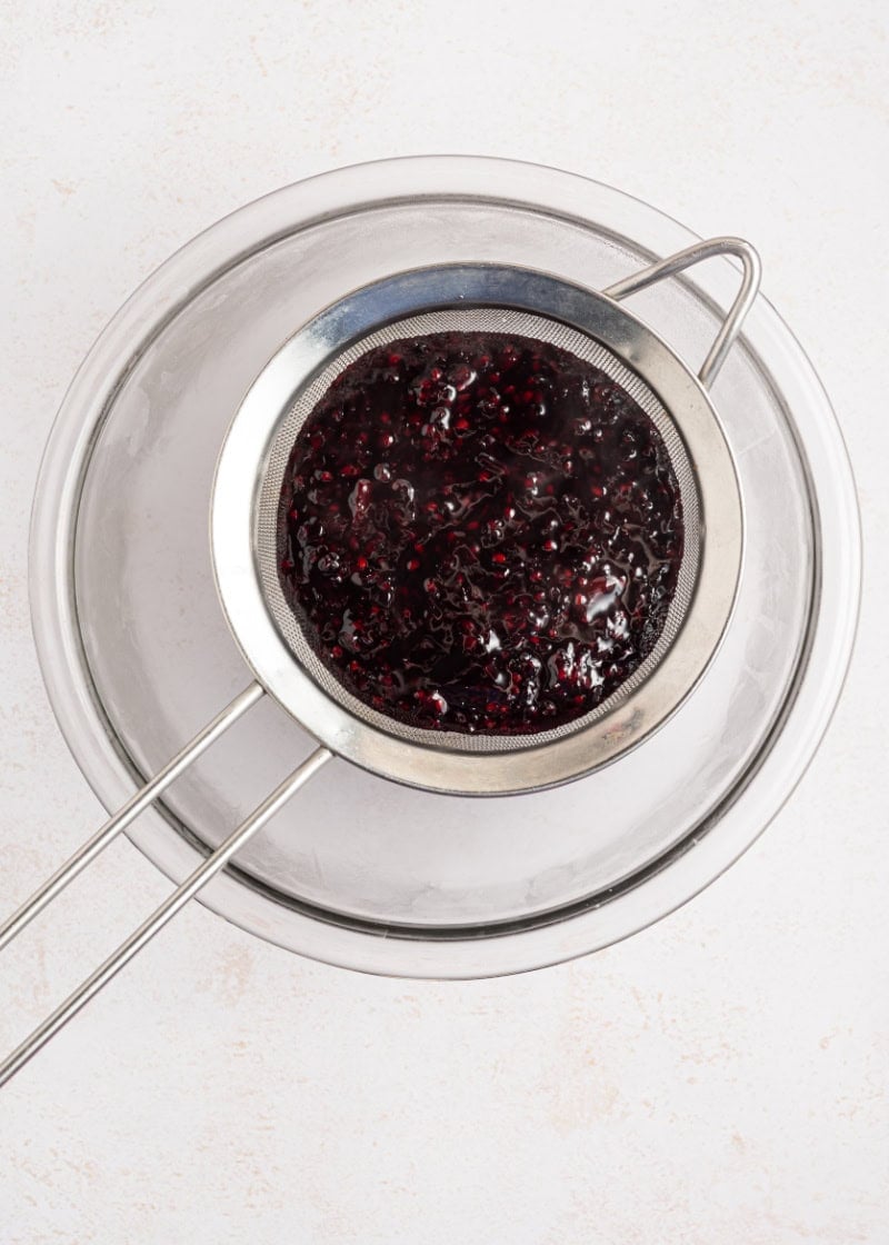 blackberry jam in a fine mesh strainer over a glass bowl.