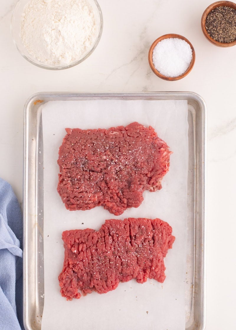 1 pieces of cube steak on a baking pan next to a bowl of flour and spices.