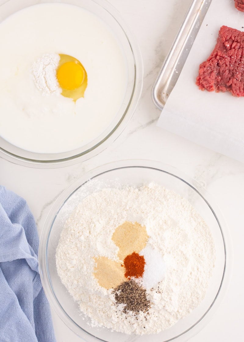 a glass bowl with milk and egg beside another glass bowl with flour and spices inside.