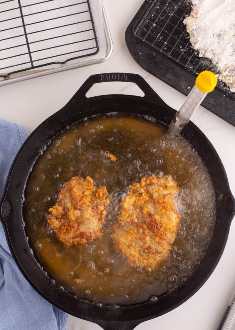 chicken fried steak cooking in a cast iron pan of oil.