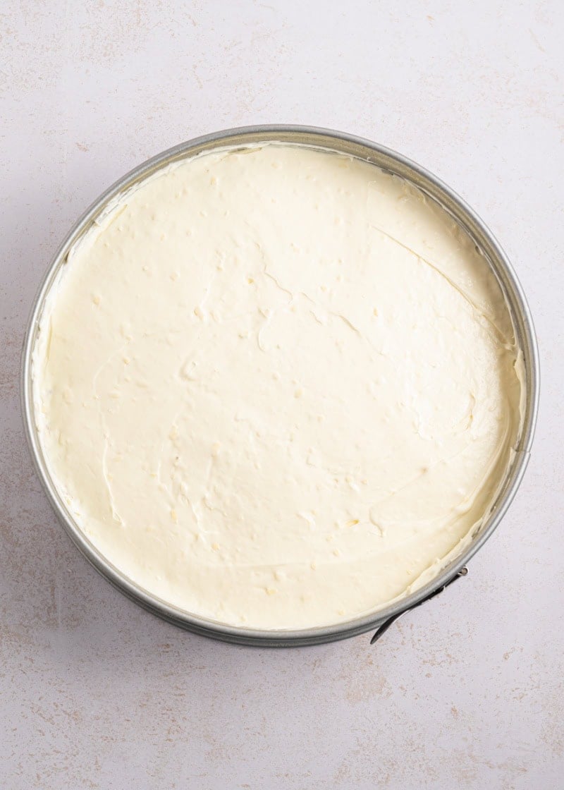 A cheesecake in a metal spring pan on table.