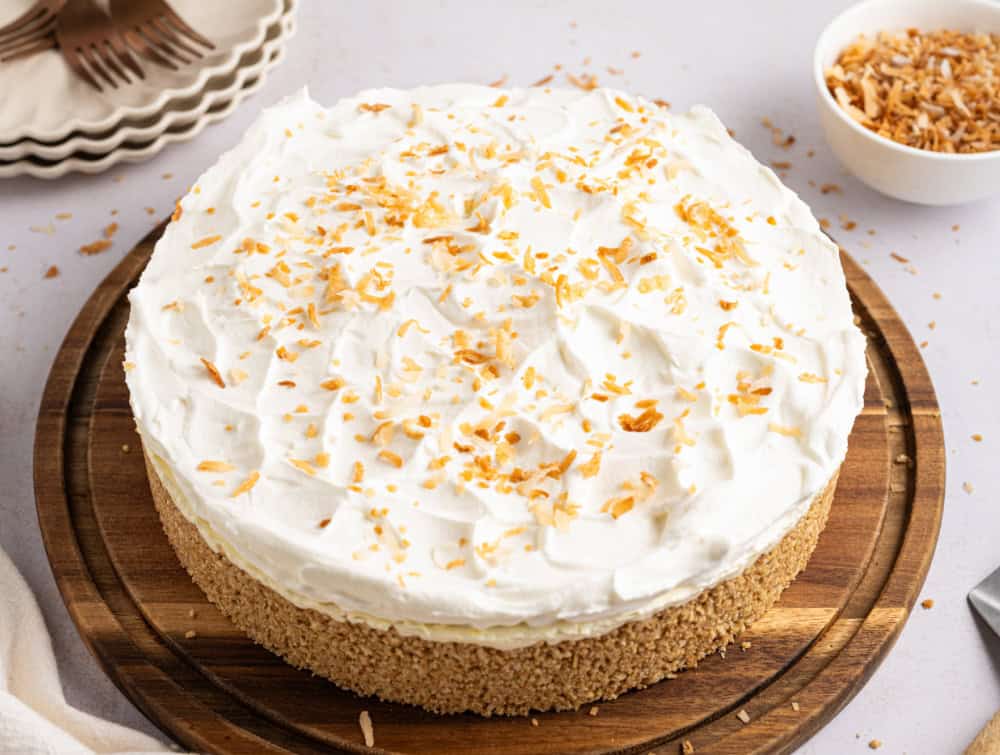 A whole coconut cheesecake with whipped cream and coconut flakes on top.
