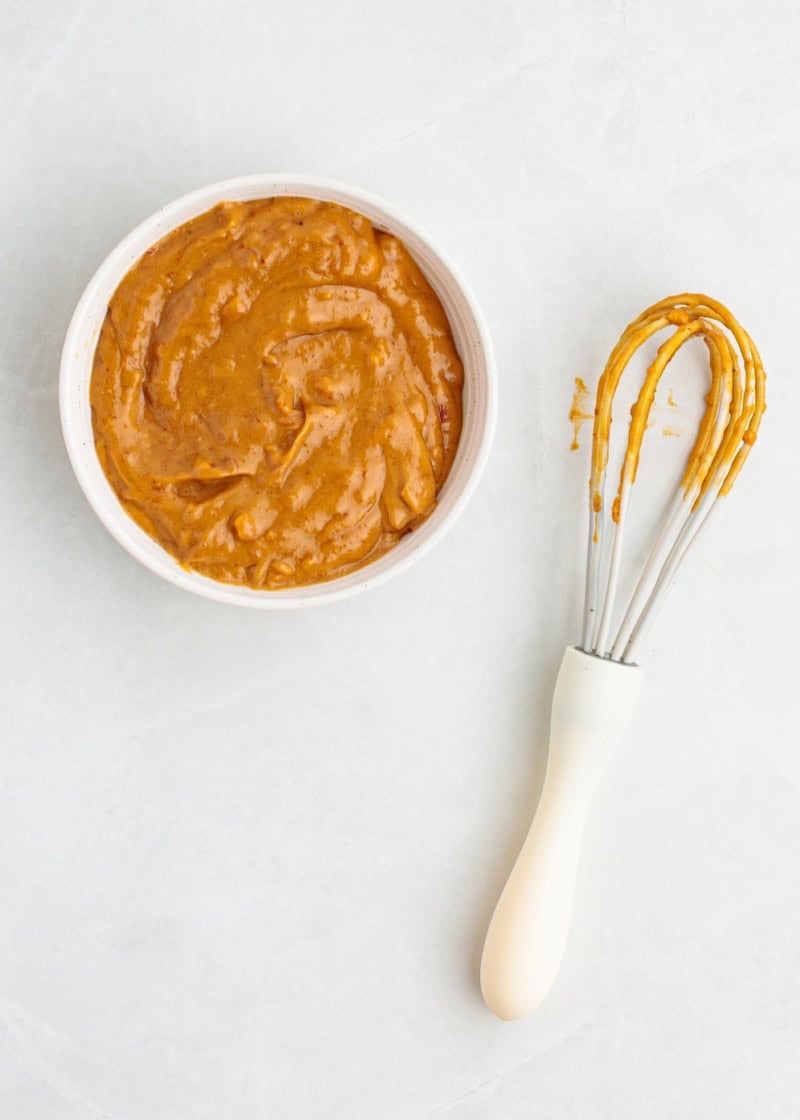 Peanut dipping sauce in a small white bowl with a whisk beside it.