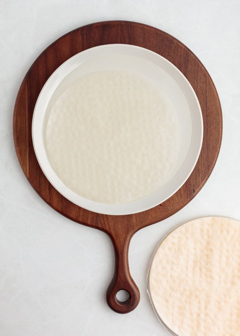 A round piece of rice paper in a shallow bowl of water.