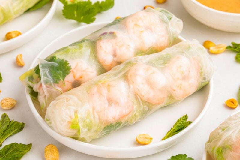 Vietnamese Shrimp Salad Rolls on a white plate with fresh herbs around it.