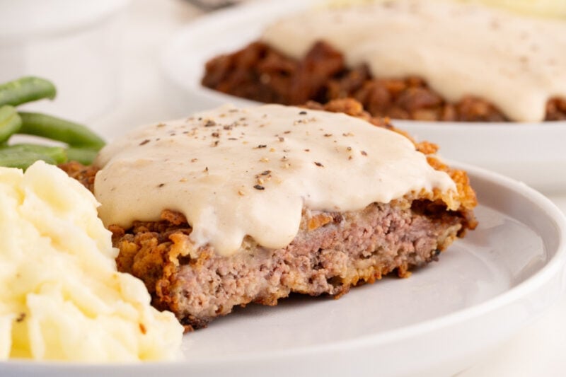 cut open chicken fried steak with gravy on top of it, on a plate with mashed potatoes and green beans.