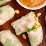 Vietnamese Shrimp Salad Rolls on a white plate with fresh herbs around it and a small bowl of peanut dipping sauce.