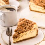 a slice of Coffee Cake Cheesecake on a white plate with a fork beside it.