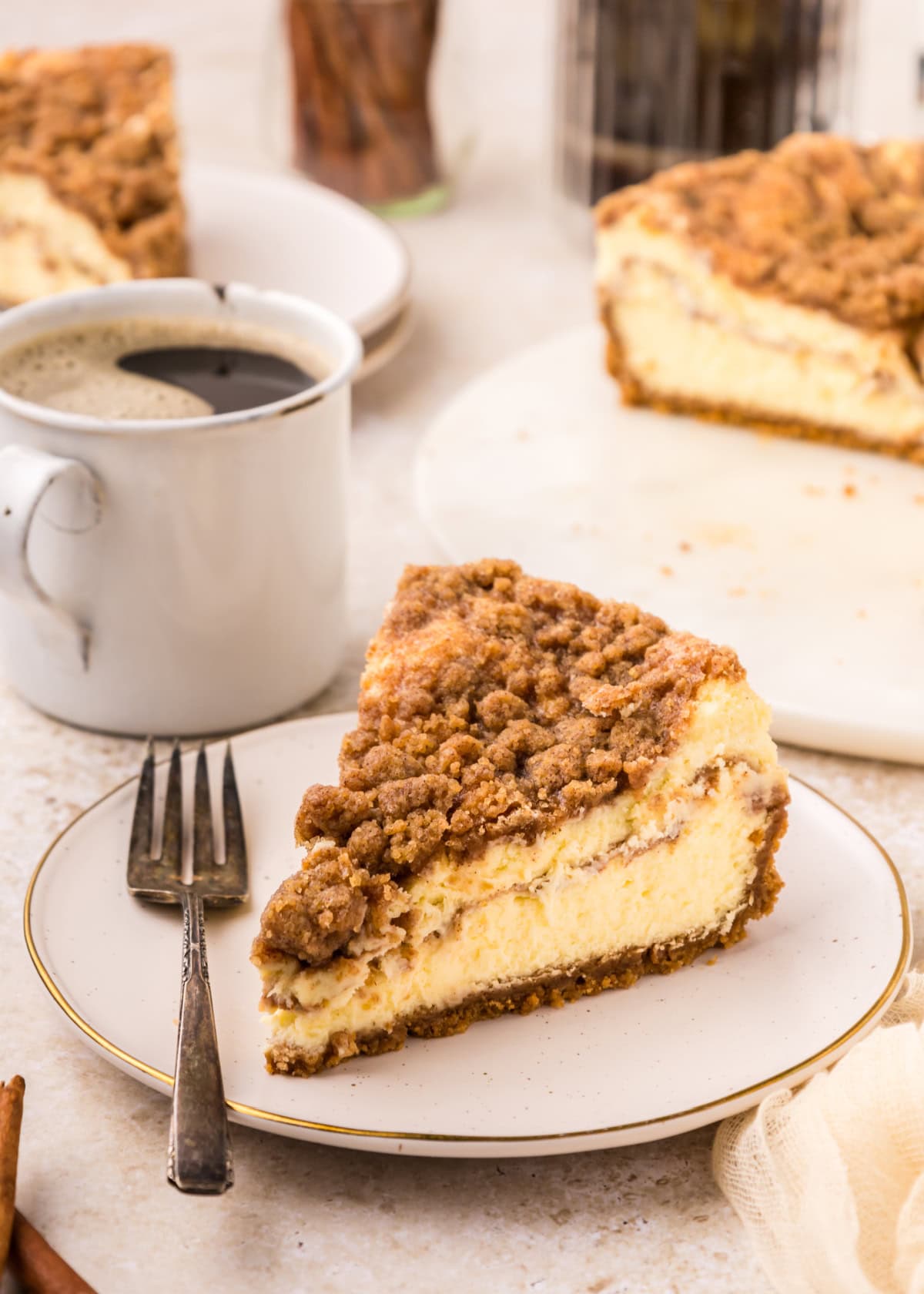 a slice of Coffee Cake Cheesecake on a white plate with a fork beside it.