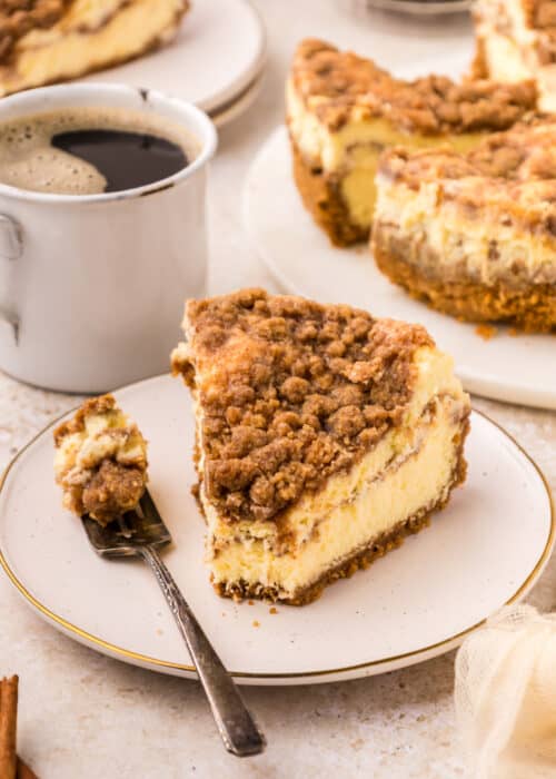 a slice of Coffee Cake Cheesecake on a white plate with a fork beside it.
