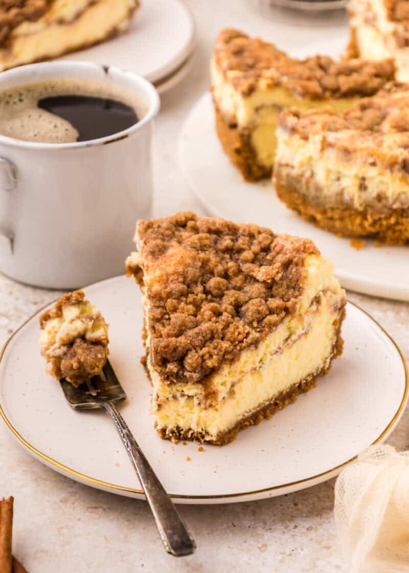 a slice of Coffee Cake Cheesecake on a white plate with a fork beside it.