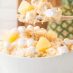 Pineapple Fluff recipe in a white bowl with some on a wooden spoon.
