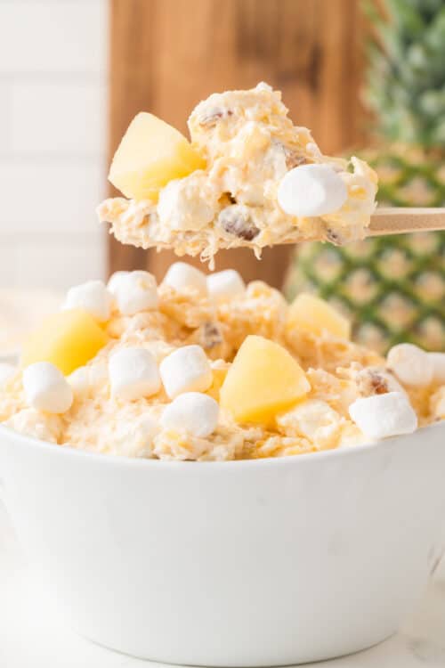 Pineapple Fluff recipe in a white bowl with some on a wooden spoon.