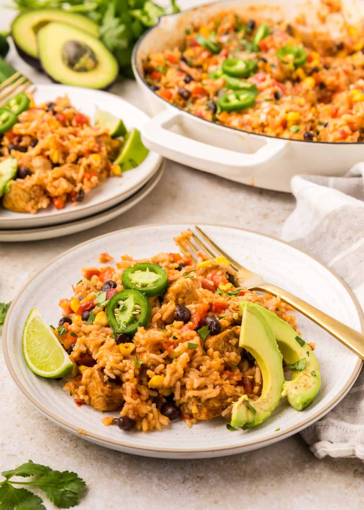 Southwest Chicken Skillet on plates with forks and fresh avocado slices beside a cooking pan.