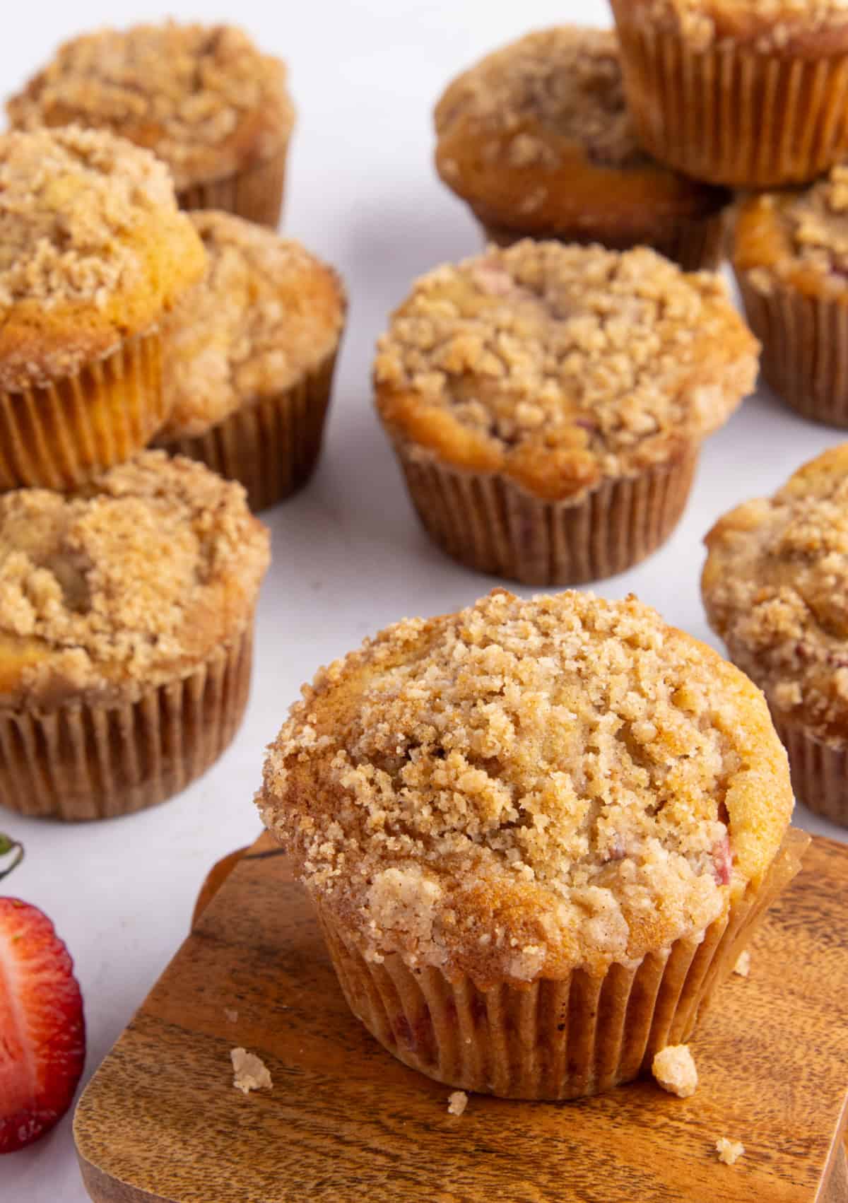 Strawberry rhubarb muffins on a white plate with a fresh strawberry slice beside them.