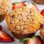 Strawberry rhubarb muffins on a white plate with fresh strawberry slices beside them.