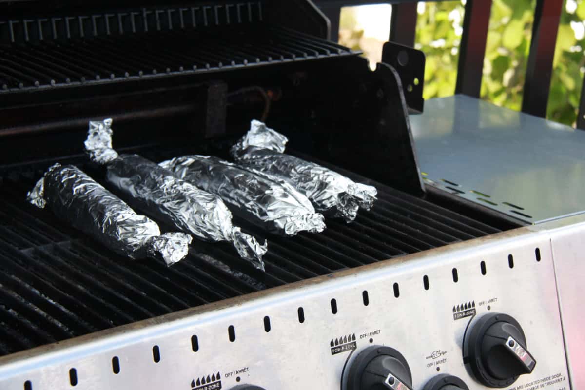 A grill with foil wrapped corn on the cob on it.