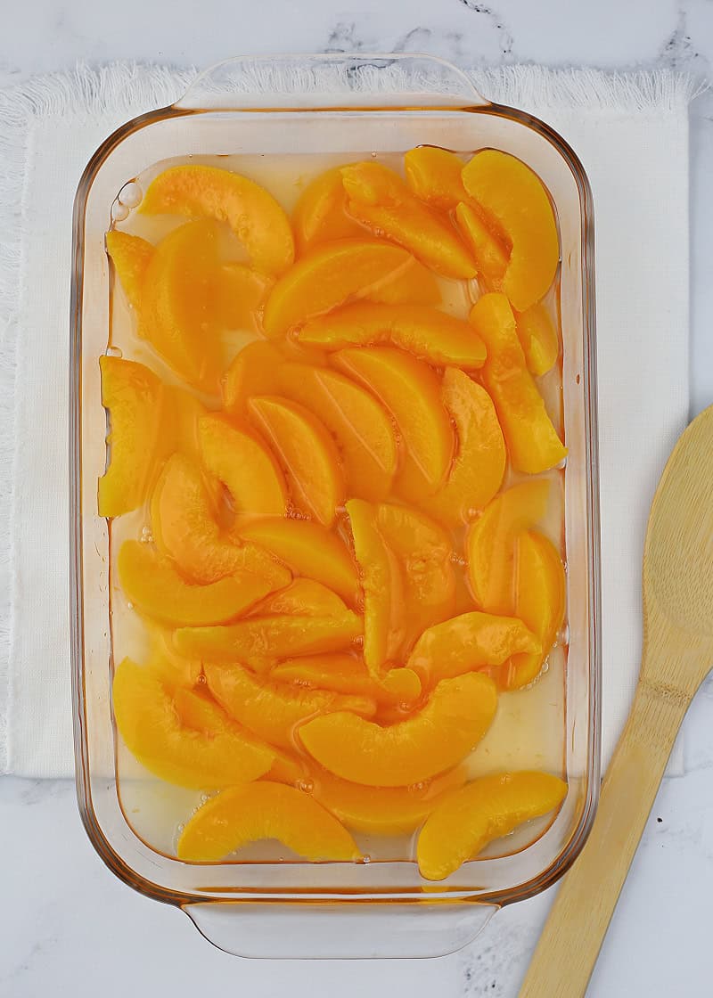 canned peaches in a glass dish with a wooden spoon.