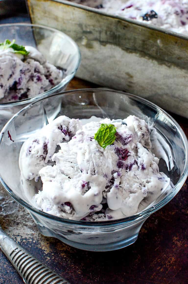 Blueberry ice cream in a bowl with a mint leaf on top.