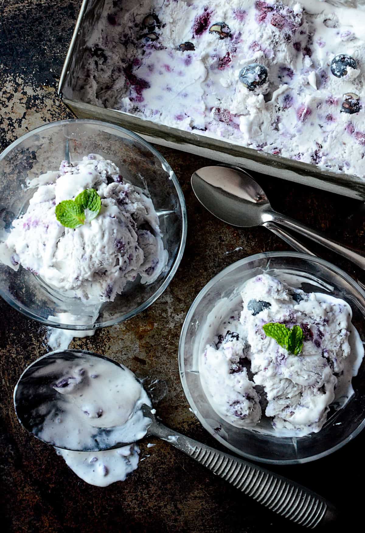 Blueberry ice cream in bowls with a mint leaf on top.