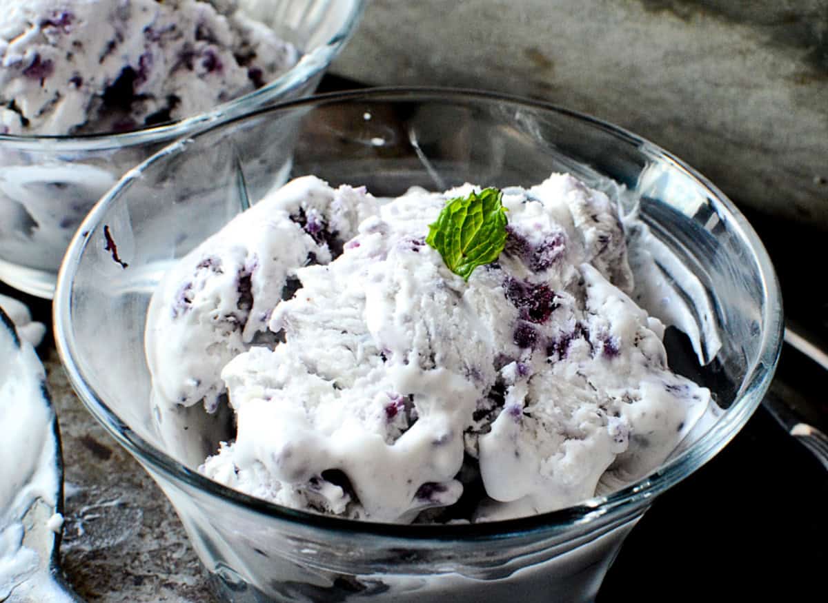 Blueberry ice cream in a bowl with a mint leaf on top.