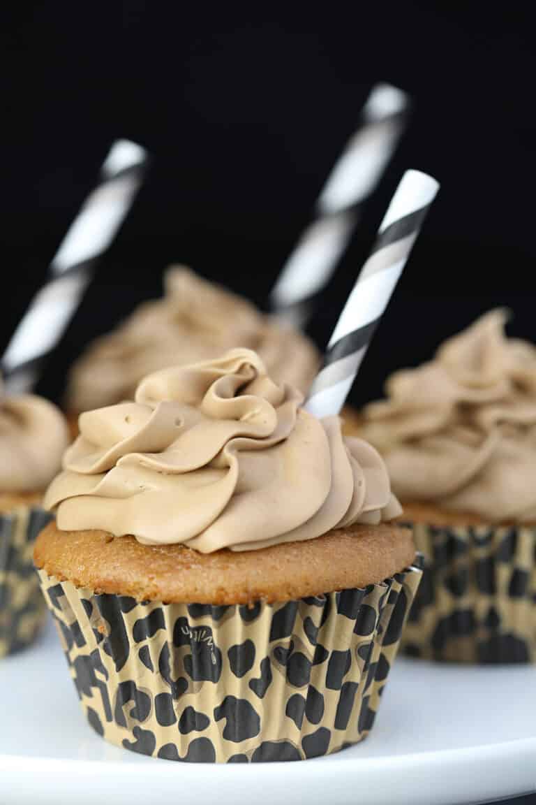 Root beer cupcakes with brown root beer frosting and a straw inserted on top, on a white plate.