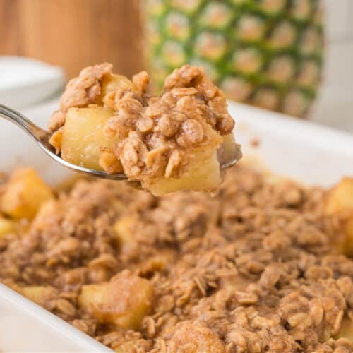 a spoon lifting pineapple crisp from a baking dish.
