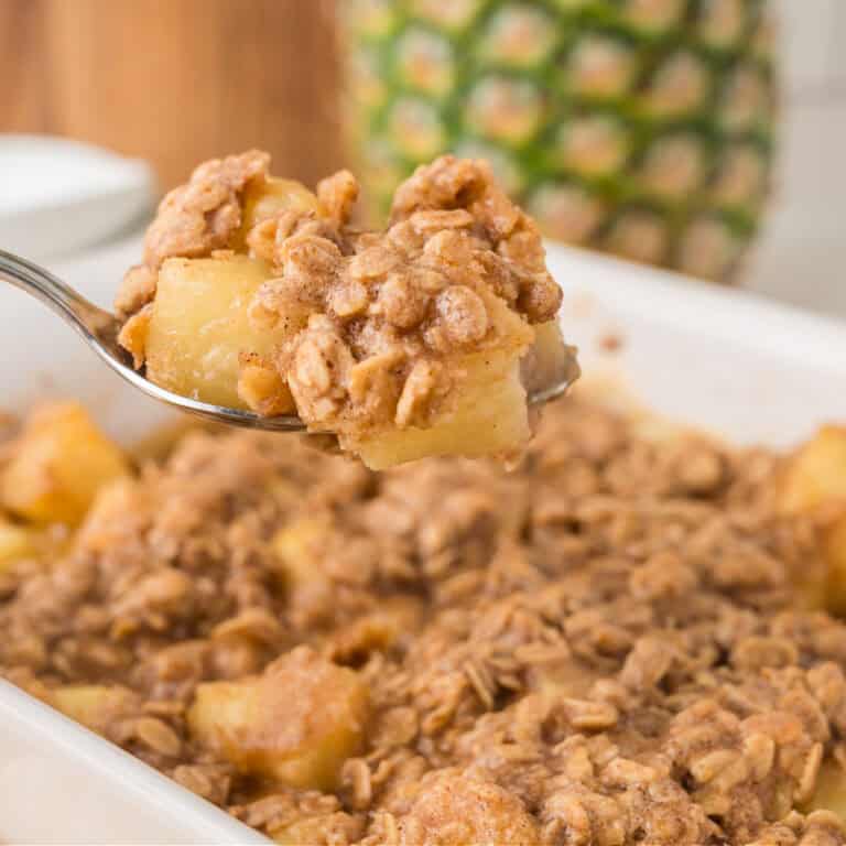 a spoon lifting pineapple crisp from a baking dish.