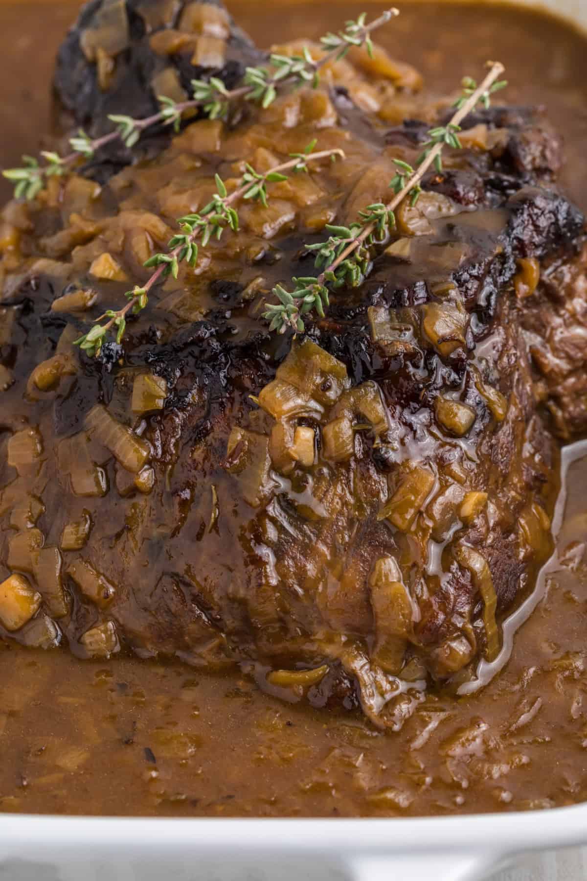 a whole french onion pot roast in a white casserole dish with dried thyme on top.