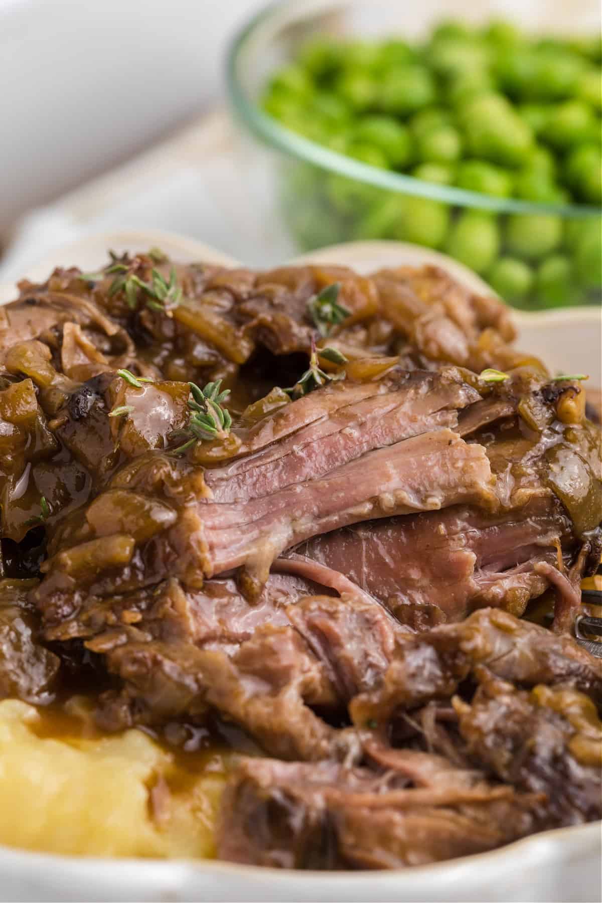 French onion beef roast over mashed potatoes and peas in a bowl beside it.