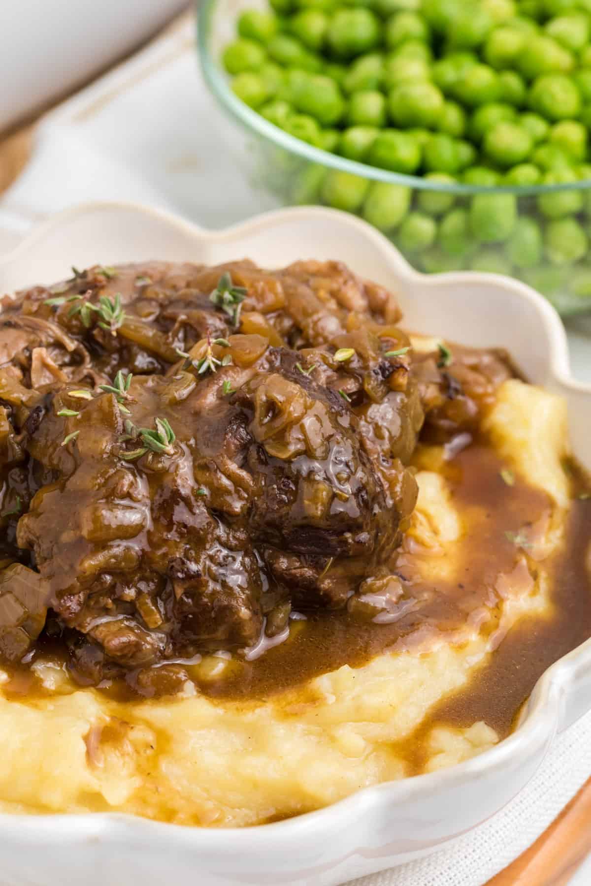 French onion beef roast over mashed potatoes and peas in a bowl beside it.